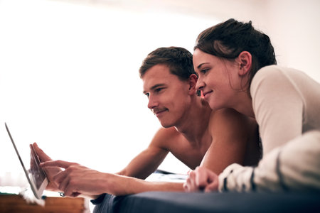Saturdays are their duvet days. a young couple spending a lazy day in bed with their tablet.の写真素材