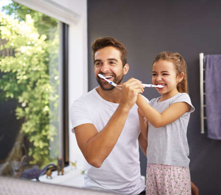 Shes learnt from the best. a handsome Dad and his daughter brushing their teeth in the bathroom at home.の写真素材
