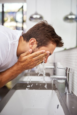The cleaner the better. Cropped close up shot of a handsome man splashing his face with water in the bathroom at home.の写真素材