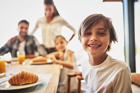 Breakfast time is the best. Portrait of a little boy having breakfast with his family in the background.の写真素材