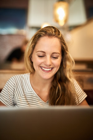 Lets get this essay started. a happy young student using her laptop to study at a cafe table.の写真素材