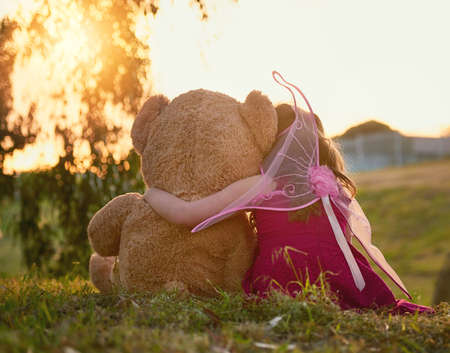 Teddy is her best friend. Rearview shot of a cute little girl playing with a huge teddybear in the park.の写真素材