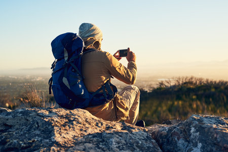 It takes time to capture the perfect picture. a hiker on top of a mountain taking a photo with his cellphone.の写真素材