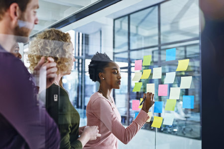 Finding ways to turn their challenges into opportunities. a team of designers brainstorming with notes on a glass wall in an office.の写真素材