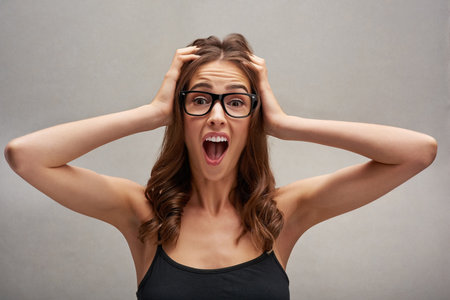 Oh no. Studio portrait of an attractive young woman looking shocked with her hands in her hair against a grey background.の写真素材