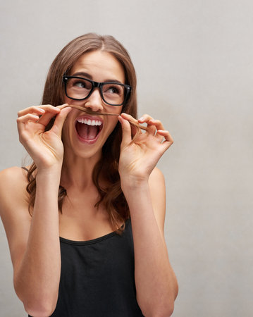 I could pull off a moustache...Studio shot of an attractive young woman posing with her hair over her lip against a grey background.の写真素材