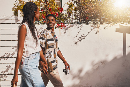 Young love couple walking in summer, sun and fresh outdoor air together in neighborhood with lens flare. Happy, smile and content black people holding hands to relax, support and enjoy quality timeの写真素材