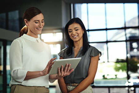 Take a look...two young businesswomen looking over a tablet in the office.の写真素材