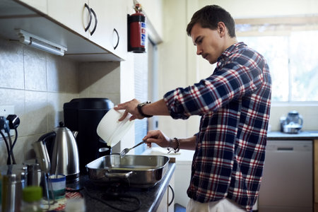 Cooking up something in the kitchen. a handsome young man cooking in the kitchen at home.の写真素材