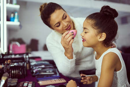Girls never stop playing dress up. a mother applying makeup to her cute little girl in a dressing room.の写真素材