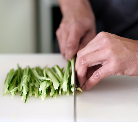 Steady hands required. an unidentifiable young man slicing vegetables in his kitchen.の写真素材
