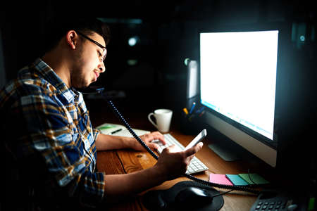 Ill be home soon...a designer reading a text message while working at his computer late in the...