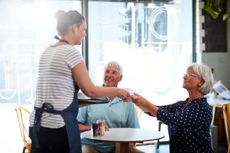 The service here is friendly and efficient. a senior couple being served by a waitress.の写真素材