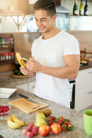 Eating a clean and light breakfast is vital. a young man making a fruit salad in his kitchen.の写真素材