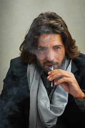 Cutting back on my nicotine intake. a stylishly dressed man smoking an electronic cigarette while...