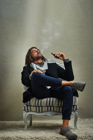 Smoking never looked this cool. a stylishly dressed man smoking an electronic cigarette while...