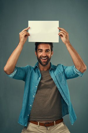 Ive saved this space just for you. Studio portrait of a handsome young man holding a blank placard against a grey background.の写真素材