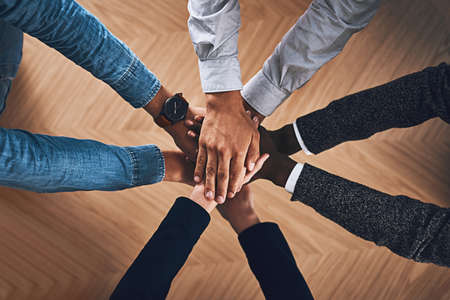 Igniting the spirit of collaboration. High angle shot of a group of unidentifiable businesspeople joining their hands together in unity.の写真素材