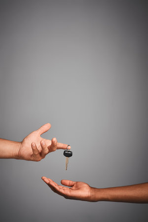 Here, you drive. Studio shot of unidentifiable hands exchanging keys against a gray background.の写真素材