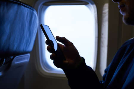Switching his phone to airplane mode. an unidentifiable passenger using his cellphone inside an...