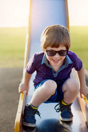 He loves coming to the playground. Portrait of an adorable little boy playing on a slide at the park.の写真素材