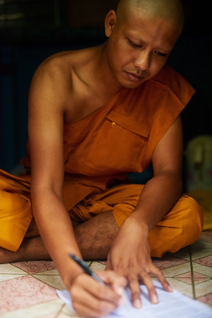 Nirvana comes tomorrow, today I need insurance. a buddhist monk filling in a form while sitting in the doorway of his home.の写真素材