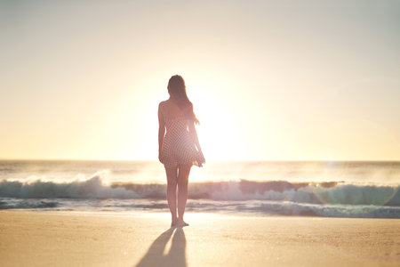 Find your freedom. Rearview shot of a young woman standing on the beach.の写真素材