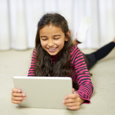 Theres always something new to entertain her online. a cute little girl using her tablet while lying...