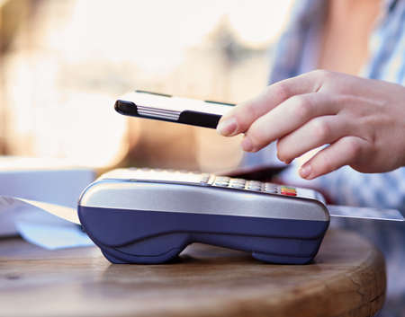 Paying is as easy as 1,2,3. an unidentifiable woman making a mobile payment with her smartphone and a card machine at a cafe.の写真素材