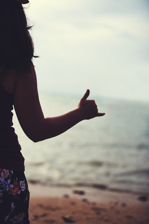 Surfs up. Rearview shot of a young woman at the beach gesturing hang ten.の写真素材