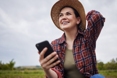 Agriculture, nature and 5g connection by farmer texting on a phone, reading social media while relaxing outdoors. Happy worker browsing the internet for natural sustainability tips, products onlineの写真素材