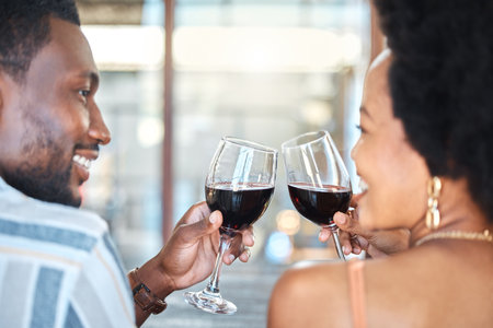 Couple giving cheers, toast and celebrate with wine glass, champagne and alcohol drinks on a romantic date together. Love, relax and smile black people in celebration of happy marriage relationshipの写真素材