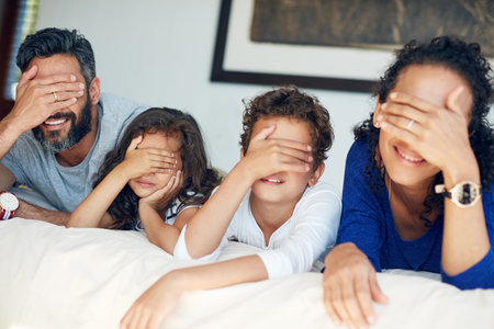 What surprise will the weekend hold for us. a family covering their eyes while lying down on a bed at home.の写真素材