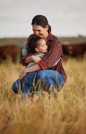 Love, family and care with a mother and daughter hugging in a field outside on a farm. Cattle farmer and little girl in the farming, agricultural and dairy industry on a meadow or pasture outdoorsの写真素材