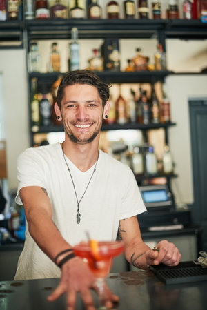 You got served. Portrait of a happy young bartender serving a cocktail behind the bar.の写真素材