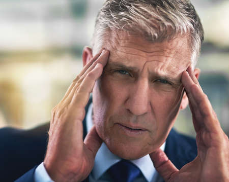 All this tension is giving me a headache. Portrait of a tense businessman holding his head in the...