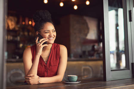 What are you doing this weekend Lets make plans. a young woman talking on a cellphone in a cafe.の写真素材