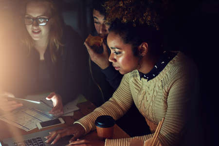 Working against a deadline. a business team using a laptop together on a night shift at work.の写真素材