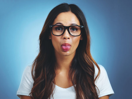 Feeling her silly mood take over. Studio portrait of an attractive young woman sticking her tongue out against a blue background.の写真素材