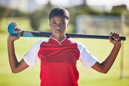 Hockey player or coach holding stick ready for a competition or match on the sports ground or field. Portrait of a serious, fit and active black woman athlete at fitness training, exercise or workoutの写真素材