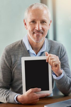 If youre in business, then you NEED one of these. Portrait of a mature businessman showing you his digital tablet in the office.の写真素材
