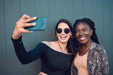 Happy girl friends taking a selfie on phone while traveling around the city on summer vacation. Diversity, love and smiling women taking picture on smartphone to post on social media and the internetの写真素材
