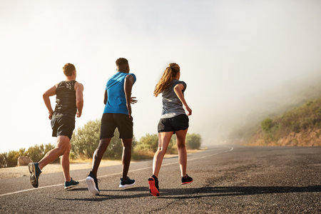 Running towards a better life. Rear view shot of a group of sporty young people out for a run together.の写真素材