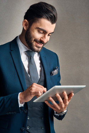 Hes one smart businessman, in both senses of the word. Studio shot of a stylishly dressed young businessman using a digital tablet against a grey background.の写真素材
