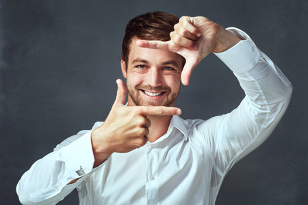 Now theres a face Id like to capture. Studio portrait of a handsome young man framing with his fingers against a dark background.の写真素材