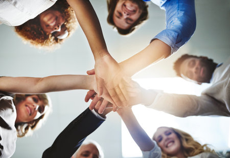 When we go all in we all win. Low angle shot of a group of colleagues joining their hands in...