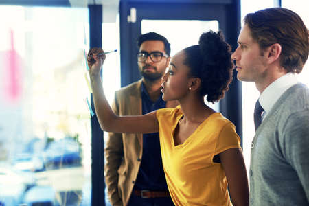Developing a plan of action. a group of businesspeople brainstorming with notes on a glass wall in an office.の写真素材