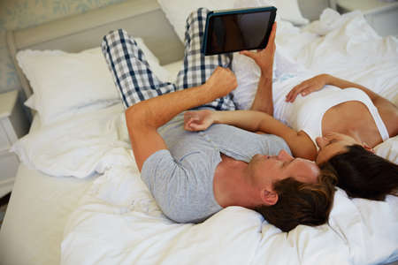 Sharing their online interests with each other. a mature couple using a digital tablet while relaxing in bed together.の写真素材