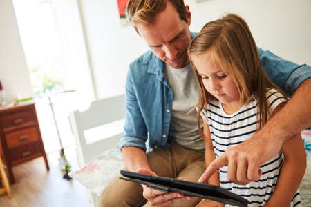Teaching her about technology. a father and his young daughter sitting together in the living room at home using a digital tablet.の写真素材