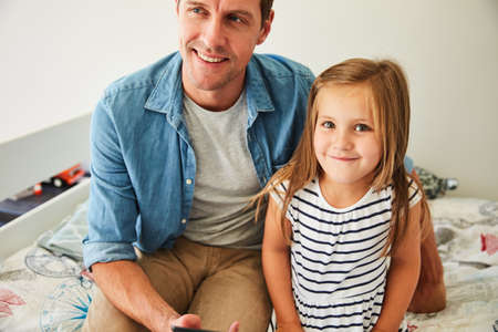 Father and daughter bonding. Portrait of a smiling little girl sitting with her father at home.の写真素材